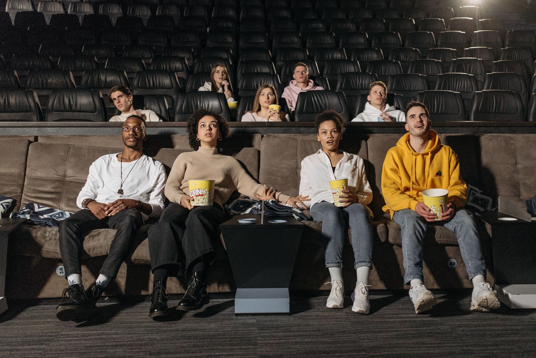 couples with fear reactions sitting on brown couch holding buckets of popcorns